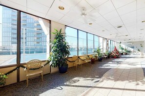 A spacious indoor area with large windows, a ceiling fan, and potted plants. - Bright coastal condo with pool access, side views of the ocean, balcony & W/D (Ocean City)