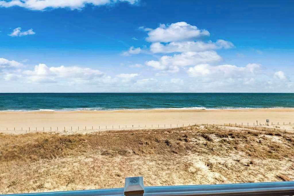 A beach with a fence, a grassy area, and the ocean.