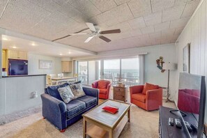 Ein Wohnzimmer mit Sofa, Sesseln, Couchtisch, Fernseher und Deckenventilator.