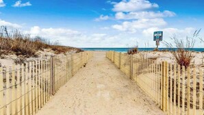 En sandstig som löper längs stranden, med trästaket på vardera sidan, och som leder ner till havet.