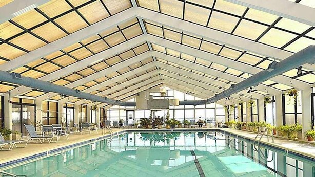 En indendørs swimmingpool med højt til loftet og ovenlys, omgivet af liggestole og potteplanter.