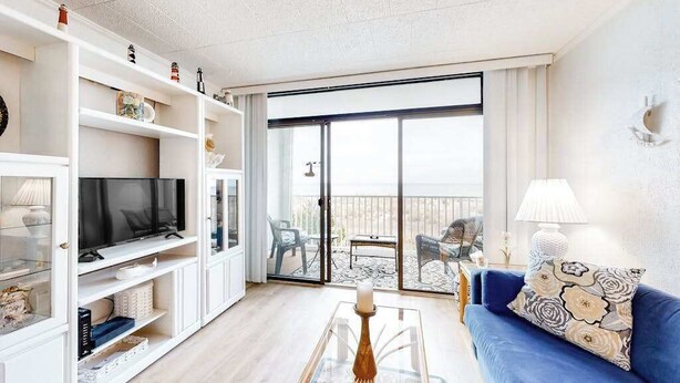 Ein Wohnzimmer mit Fernseher, Regalen, einer Couch und einem Balkon mit Gartenmöbeln.