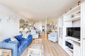Een moderne woonkamer met een blauwe bank, een witte tv-kast en een televisie.
