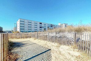A building with multiple floors, a sandy path leading to it, and a wooden fence. - Breakaway East 409 (Ocean City)