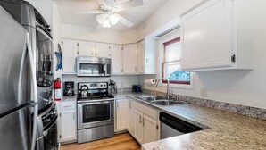 A modern kitchen with stainless steel appliances, white cabinets, granite countertops, and a ceiling fan.