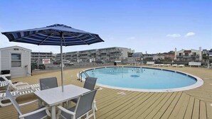A pool area with a table and chairs, a striped umbrella, and a view of buildings in the background.