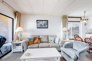 Ein Wohnzimmer mit einer Couch, zwei Beistelltischen, einem Couchtisch, einem Sessel und einem Fenster mit Vorhängen.