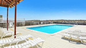 A pool area with lounge chairs, a wooden deck, and a white fence. - Beachloft 4F (Ocean City)