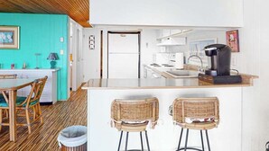 A kitchen with a central island, a dining area with chairs, and a teal wall. - Beachloft 4F (Ocean City)