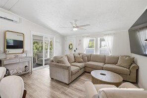 A living room with a sectional sofa, a coffee table, a TV, and a ceiling fan. - Cozy 2-bedroom mobile home in cool Fort Myers Beach with AC (Fort Myers Beach)