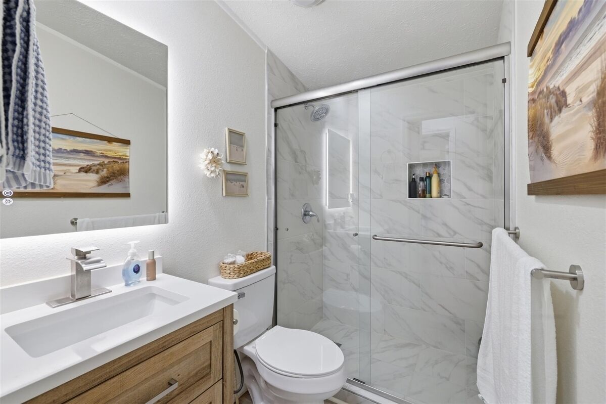 Un baño moderno con cabina de ducha de vidrio, un lavabo blanco y un inodoro.