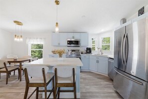 A modern kitchen with light blue cabinets, a stainless steel refrigerator, and a central island with chairs. - Cozy 2-bedroom mobile home in cool Fort Myers Beach with AC (Fort Myers Beach)
