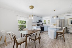 A modern kitchen with white cabinets, a microwave, a stove, and a refrigerator. There is a dining area with a wooden table and chairs. - Cozy 2-bedroom mobile home in cool Fort Myers Beach with AC (Fort Myers Beach)