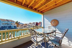 Ein Balkon mit Glastisch und Stühlen, einer Holzboden und Blick auf Gebäude und Wasser.