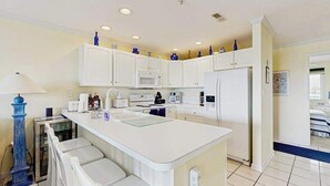 A kitchen with white cabinets, a central island, and a refrigerator. - Baywatch II 303D (Ocean City)