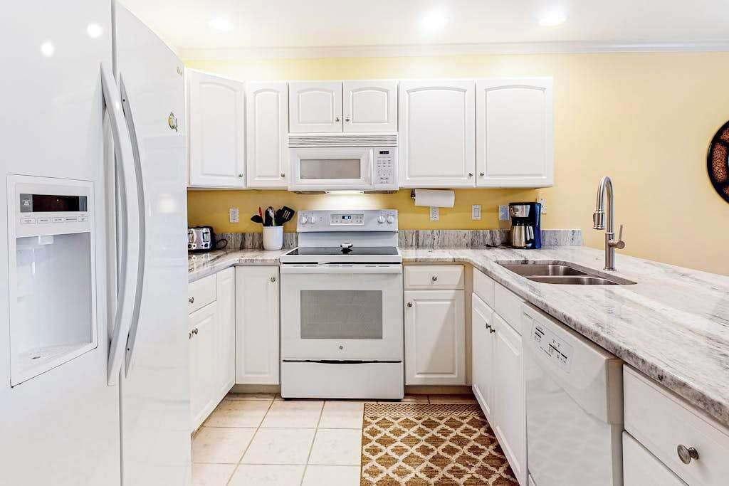 A modern kitchen with white cabinets, a microwave, stove, and a sink.