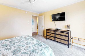 Ein Schlafzimmer mit einem Bett, einem Schminktisch, einem Fernseher und einer Tür zu einem anderen Raum.