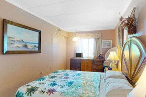 Ein Schlafzimmer mit einem Bett, einem Schminktisch, einem Fernseher und einem Bild an der Wand.