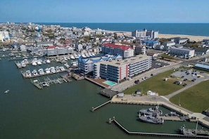 An aerial view of a coastal town with a marina, a large hotel with multiple floors, and a beach in the background.