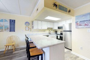 A kitchen with white cabinets, a marble island, and a painting of beach scene. - Wonderful Condo in Oceanside Building w/Free WiFi, Private Washer/Dryer (Ocean City)