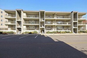 A multi-story apartment building with balconies, a parking lot, and a clear sky. - Wonderful Condo in Oceanside Building w/Free WiFi, Private Washer/Dryer (Ocean City)