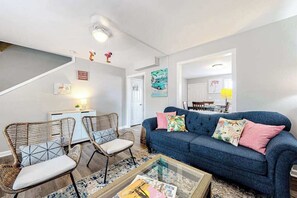A living room with a sofa, two chairs, a coffee table, and a staircase leading to another room. - Flamingo House (Ocean City)