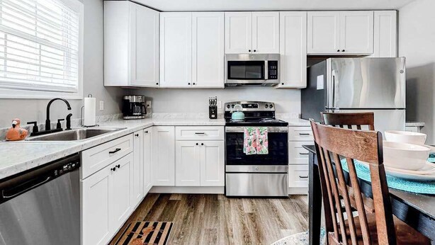 Una cocina moderna con armarios blancos, electrodomésticos de acero inoxidable y una mesa de comedor de madera.