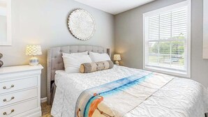 Un dormitorio con una cama, lámparas de noche, un adorno en la pared y una ventana con persianas.
