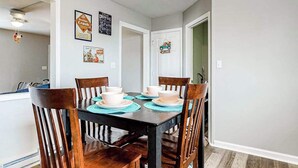 Un comedor con una mesa dispuesta para cuatro personas, sillas de madera y manteles individuales.