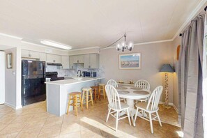 A modern kitchen with a central island, white chairs, and a dining table. - Assateague House 108 (Ocean City)