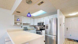 Una cocina compacta con alacenas blancas, un refrigerador de acero inoxidable, un microondas y un lavamanos.