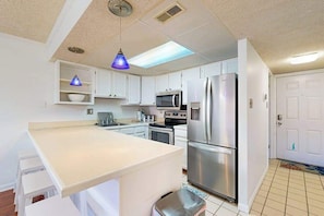 A compact kitchen with white cabinets, a stainless steel refrigerator, a microwave, and a sink. - Top-floor, corner condo steps to beach with balcony & ocean views (Ocean City)