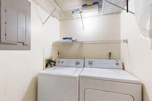 A laundry area with two stacked washers and dryers, a metal shelf above, and a door with a handle. - Top-floor, corner condo steps to beach with balcony & ocean views (Ocean City)
