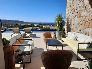 Une terrasse avec mobilier d’extérieur, une piscine et une vue sur la mer et les collines.