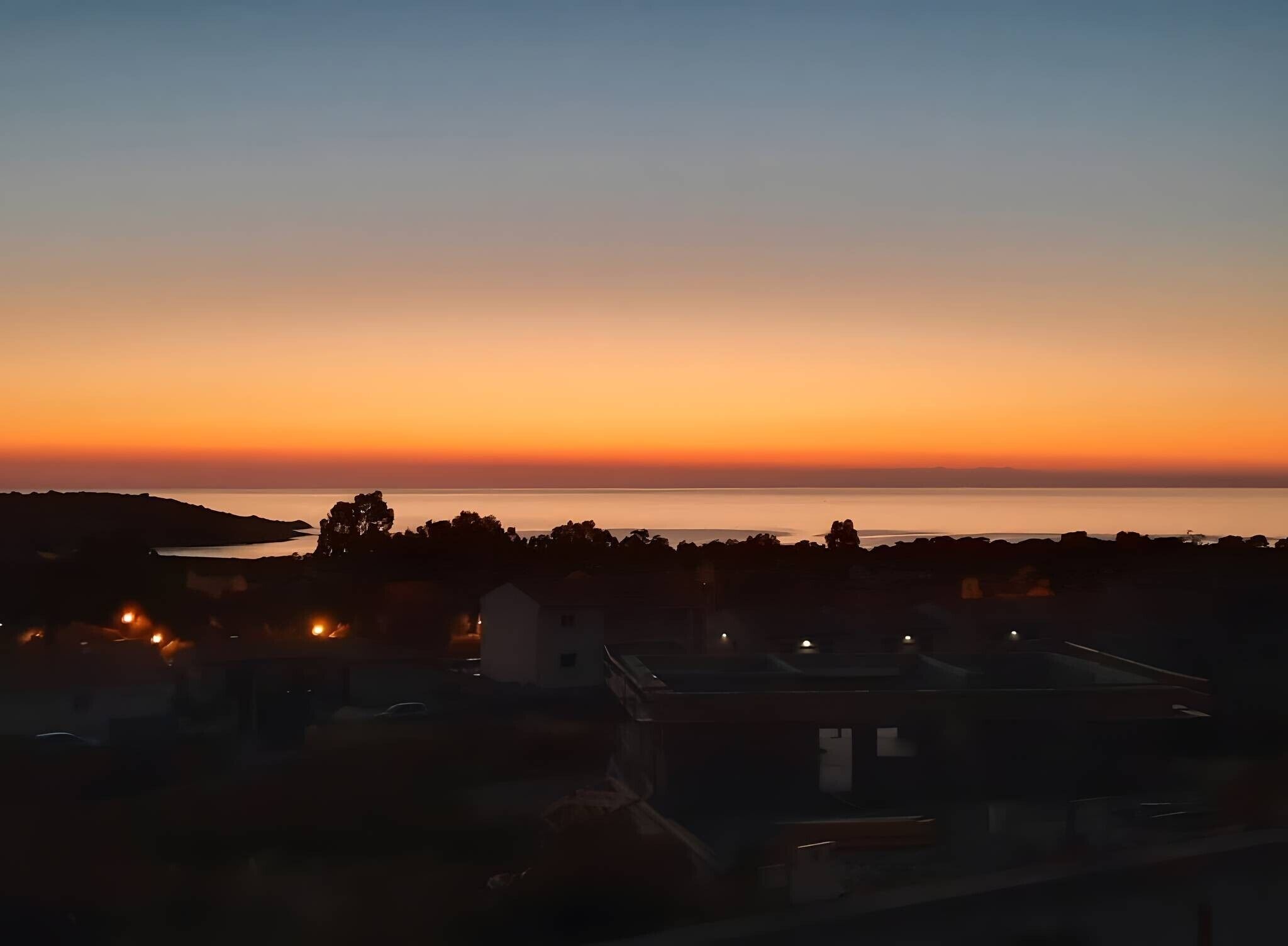 Ein Küsten-Sonnenuntergang mit gegen den Himmel abgesetzten Gebäuden.
