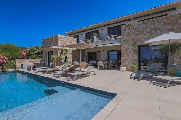 A modern house with a swimming pool, outdoor seating, and stone walls.