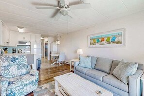 Ein modernes Wohnzimmer mit grauem Sofa, einem gemusterten Sessel, einem Couchtisch und einem Deckenventilator.