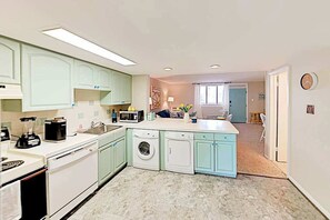 A compact kitchen with a washing machine, a microwave, and a coffee maker. - Updated Colonial Condo | Patio, Smart TV & Beach Gear | 200’ to Beach (Ocean City)
