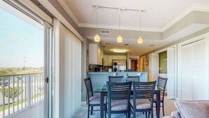 Un balcón con vistas, un comedor con sillas y una mesa, y una cocina al fondo.