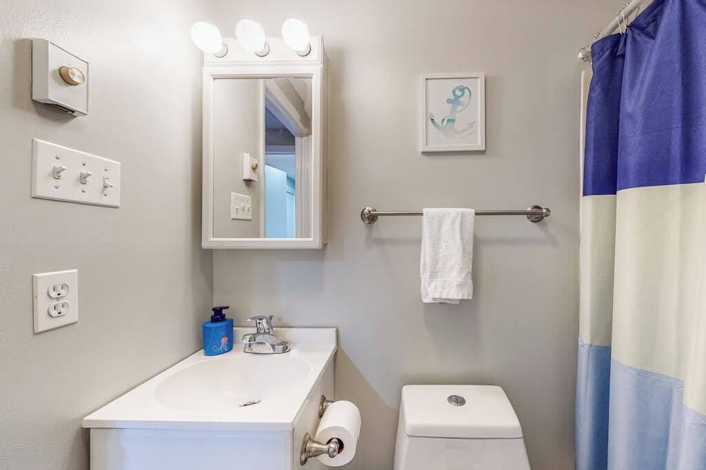 A bathroom with a white sink, a mirror with lights, a towel rack, a toilet, and a shower curtain.