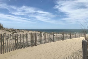 Ein Sandstrand mit einer Holzlattenveranda und einem wolkenlosen Himmel.