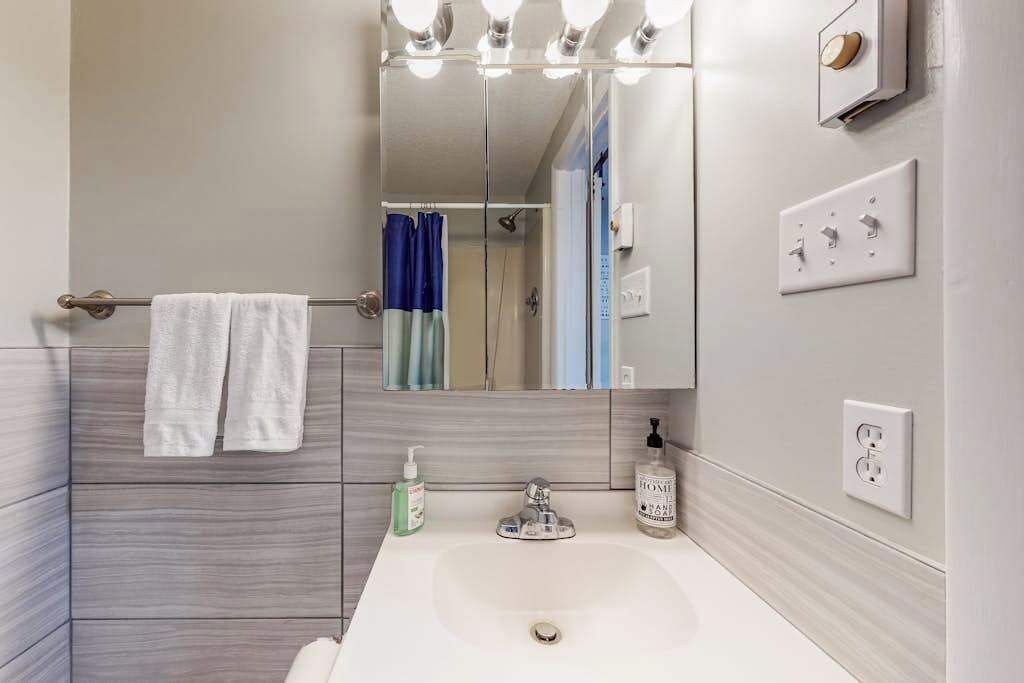 A bathroom with a mirror, towel rack, sink, and toiletries.