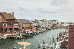 A waterfront property with docked boats, a covered area, and a row of multi-story buildings. - Canal-front townhome with front/back decks, shared pool, private w/d, & WiFi (Ocean City)