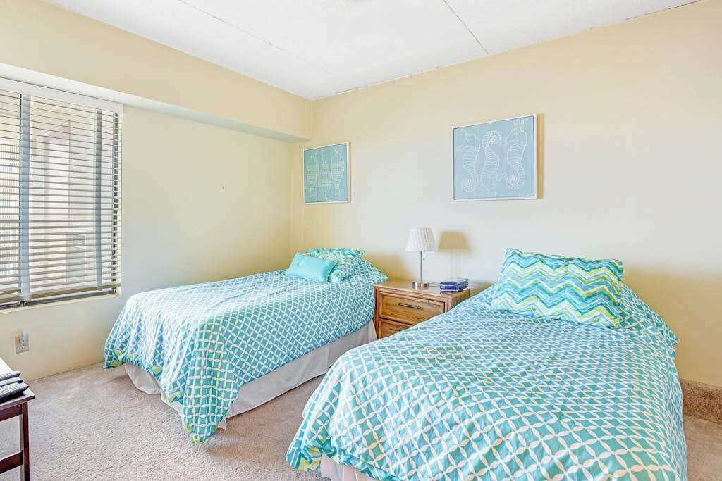 A bedroom with two beds, a nightstand, a lamp, and a window with blinds.