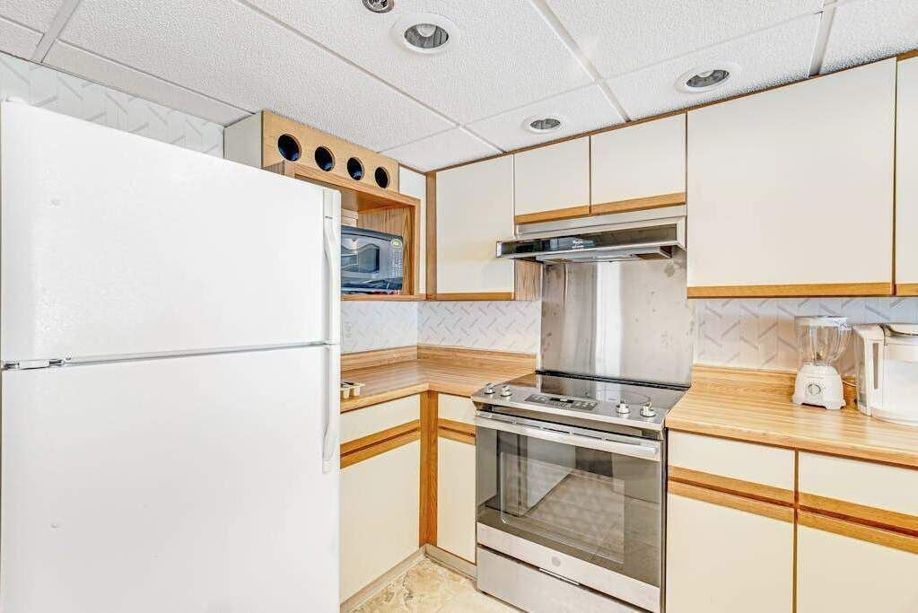 A compact kitchen with a refrigerator, microwave, stove, oven, and a blender on the countertop.