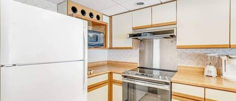 A compact kitchen with a refrigerator, microwave, stove, oven, and a blender on the countertop.
