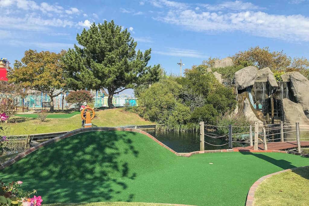 Een minigolfbaan met een putting green, een waterhindernis en een rotsformatie.