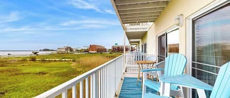 A balcony with a view of the beach, a table with chairs, and a railing.