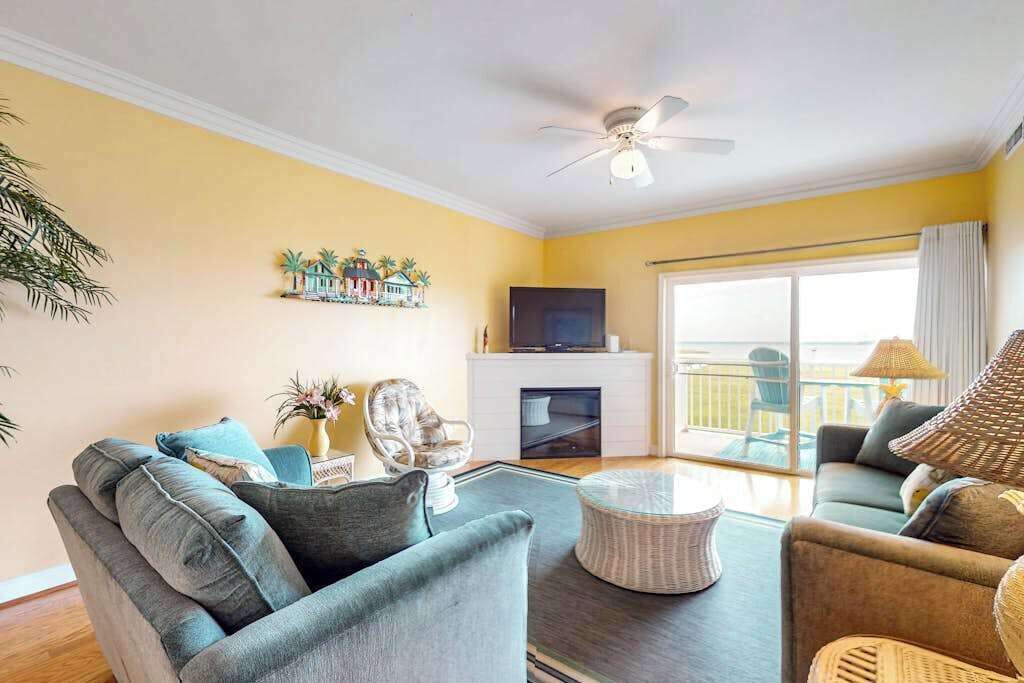 A living room with a sofa, armchair, coffee table, TV, fireplace, and a balcony with a view.