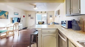A kitchen with a microwave, sink, and cabinets. There is a dining area with chairs and a table. - Condo Less than Two Miles to the Ocean with Pool, Fast WiFi, and Private W/D (Ocean City)